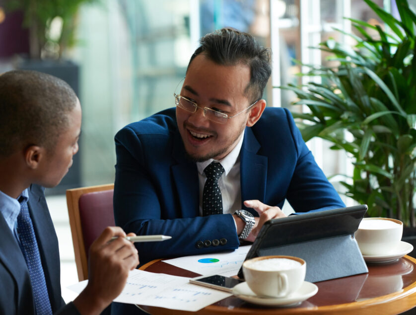 Cheerful Vietnamese businessman having meeting with African-American partner in cafe