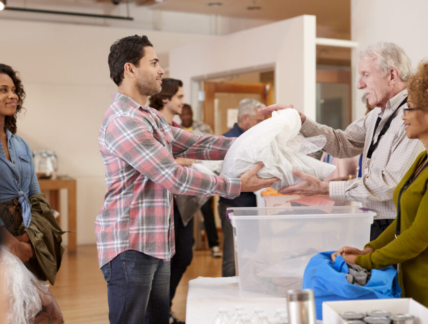 People Donating Clothing To Charity Collection In Community Center