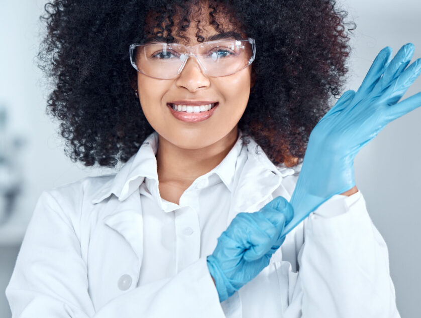 Portrait of young african american female scientist with afro hair wearing a labcoat and goggles wh.